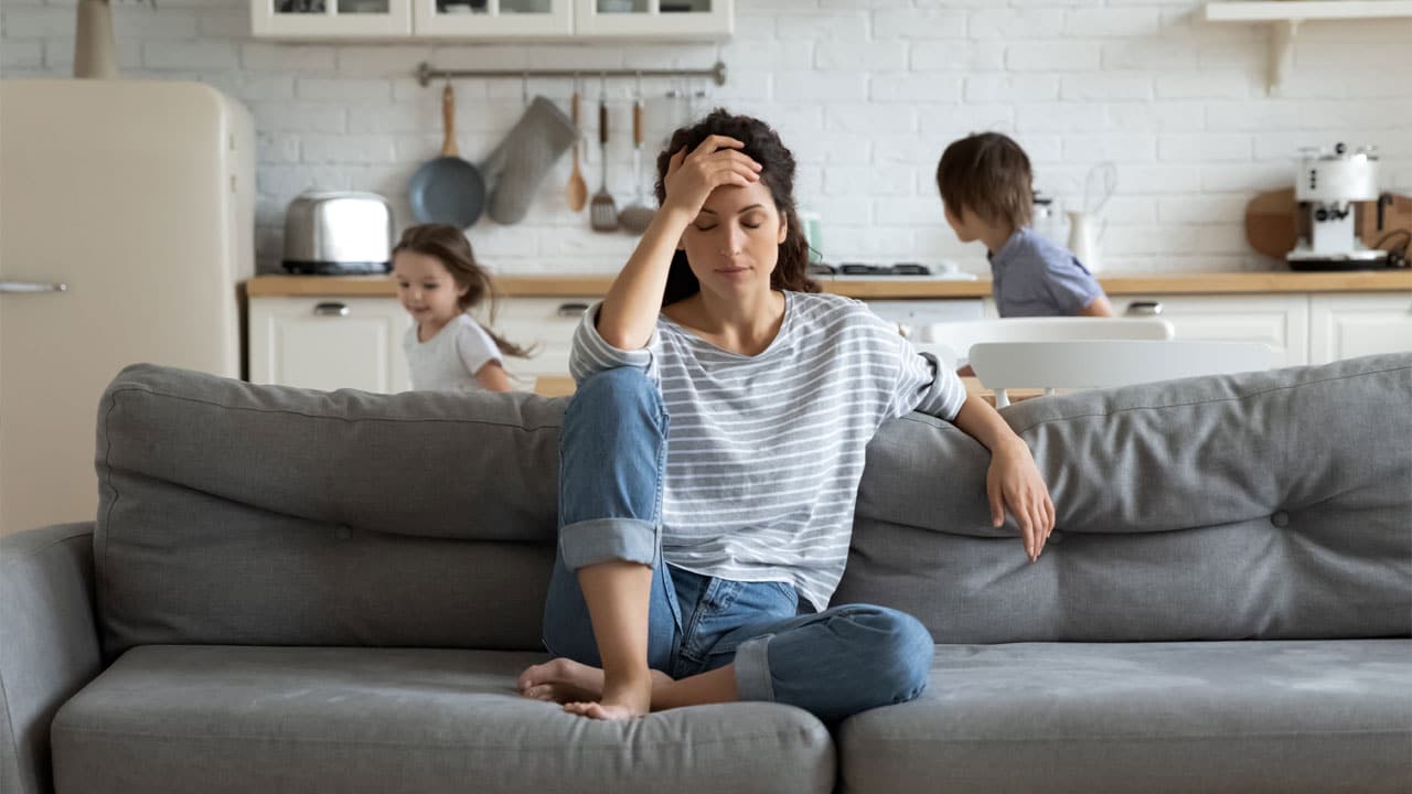 Woman showing signs of stress at home with children playing in background
