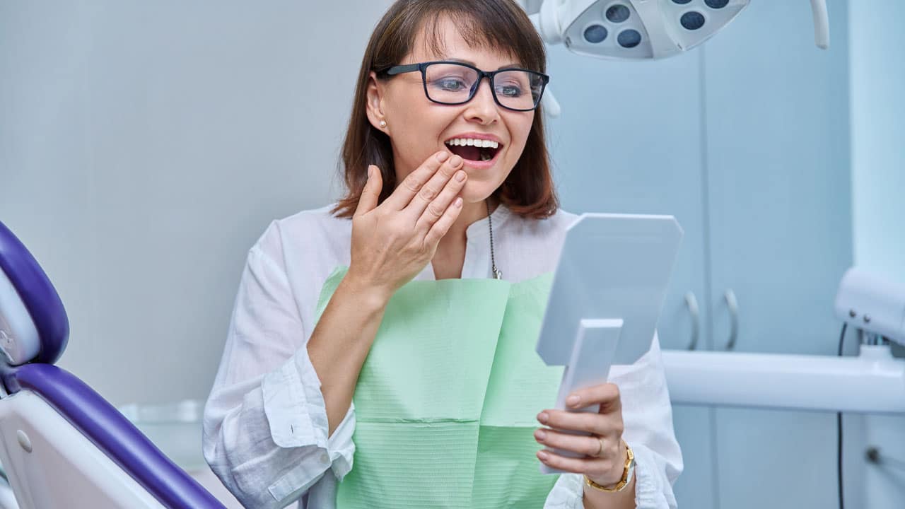 Woman in dental chair looking at teeth in the mirror